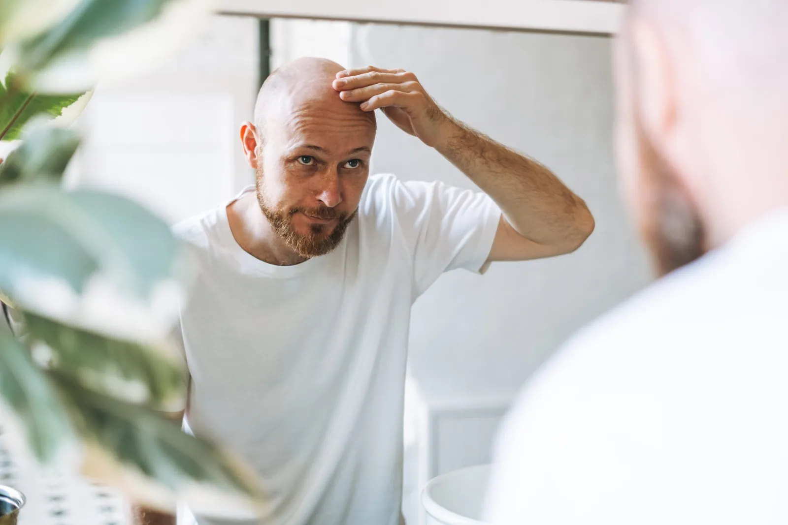 Bald man looking in a mirror and touching his forehead